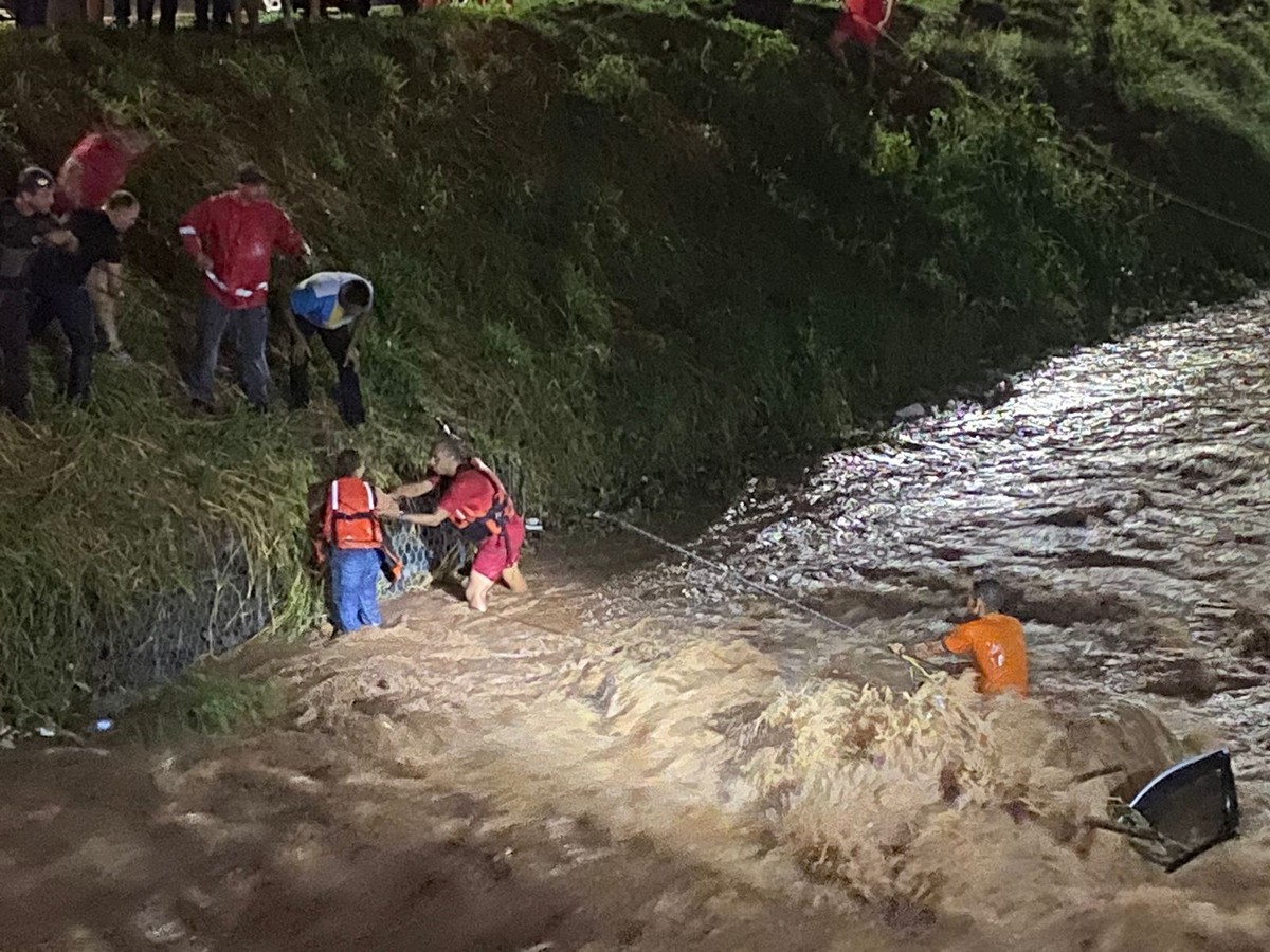 Carro com duas pessoas cai em córrego durante chuva, morador tenta ajudar e os três são resgatados pelos bombeiros em Lins